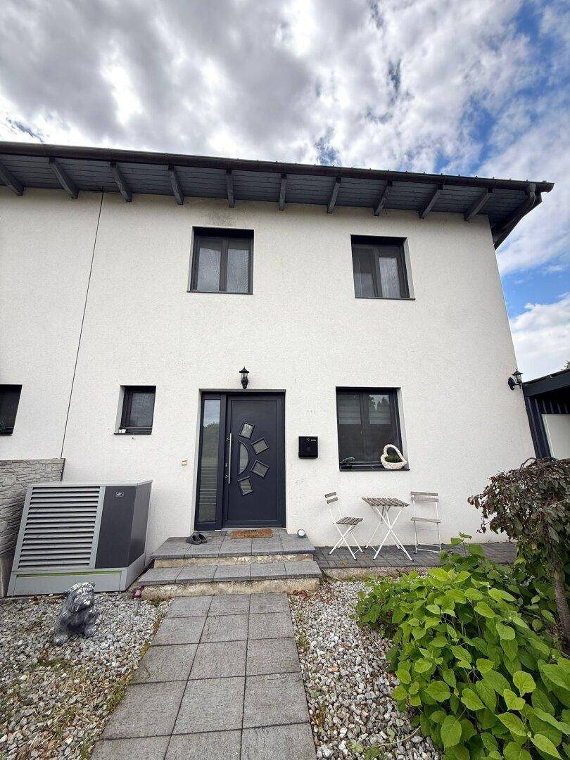 Moderne Hausfassade mit Wärmepumpe und gepflastertem Eingangsbereich.