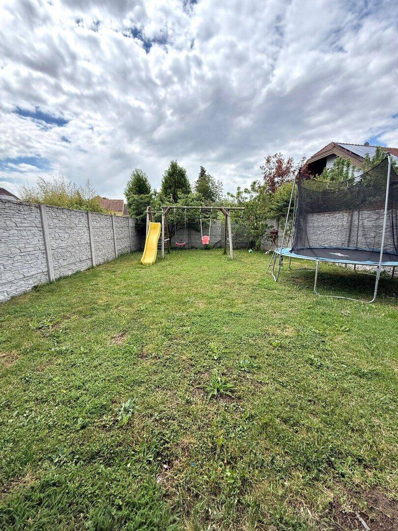Großer Garten mit Rasenfläche, Schaukel, Rutsche und Trampolin.
