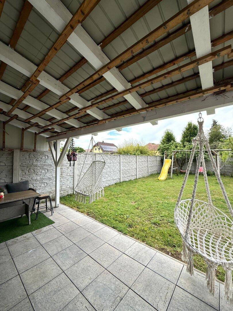 Überdachte Terrasse mit Fliesenboden, Hängesesseln und Blick in den Garten.