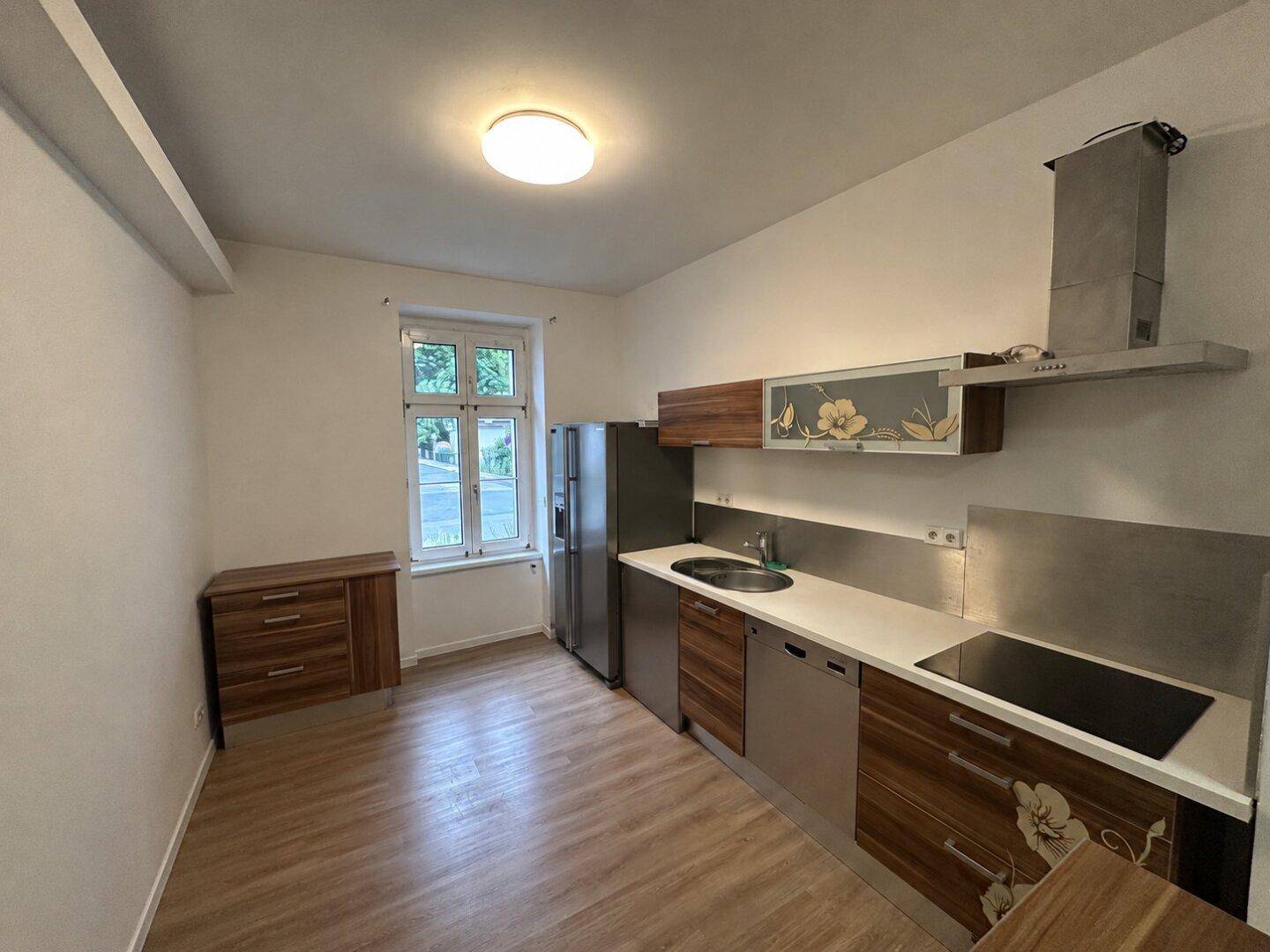 Moderne Küche mit Holzboden, Edelstahlgeräten und einem Fenster mit Blick nach draußen.