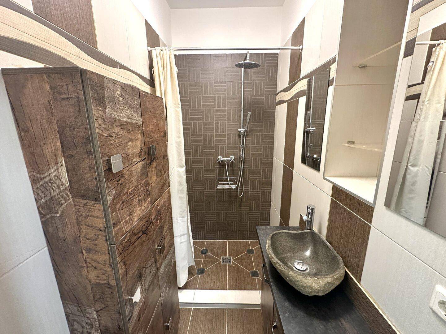Modernes Badezimmer mit Dusche, Steinwaschbecken und braunen Fliesen an den Wänden.