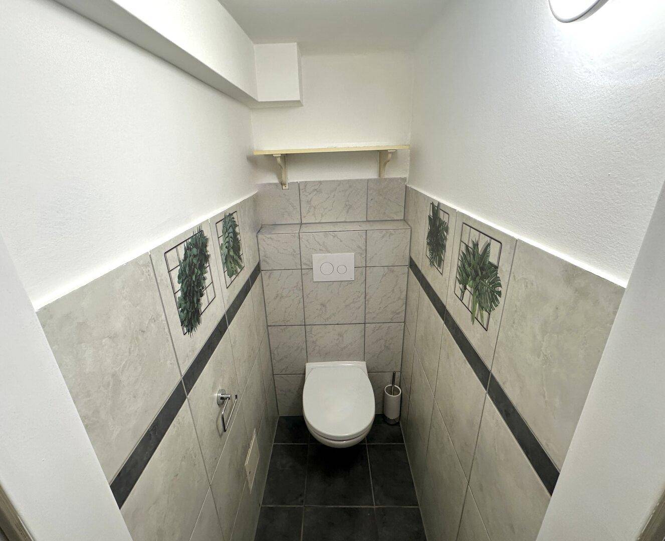 Kleines Gäste-WC mit Wand-WC und dekorativen Fliesen an den Wänden.