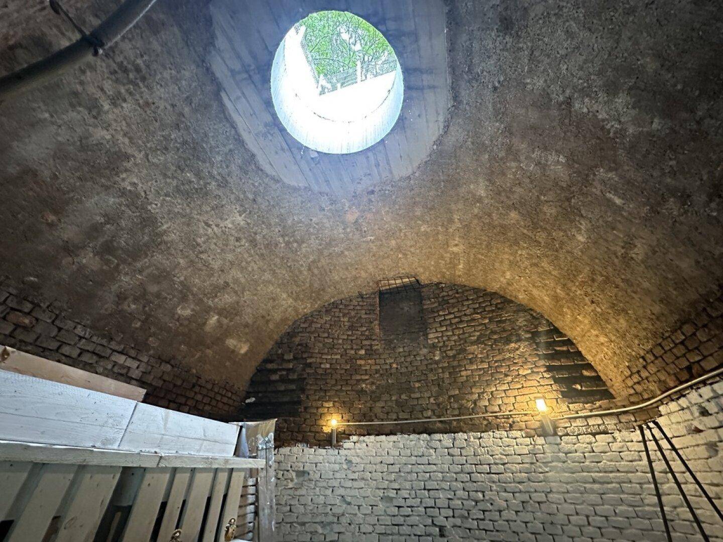 Historischer Gewölbekeller mit Ziegelwänden und einer runden Öffnung in der Decke.