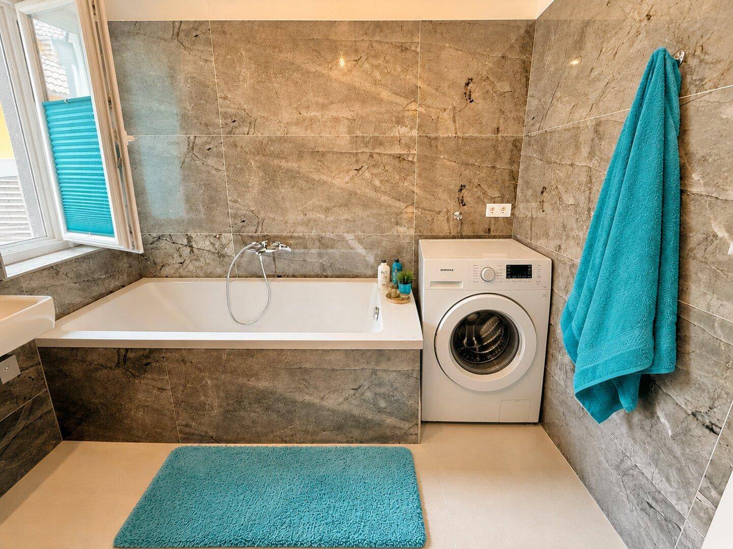 Modernes Badezimmer mit Badewanne, Waschmaschine und grauen Marmorfliesen an den Wänden.