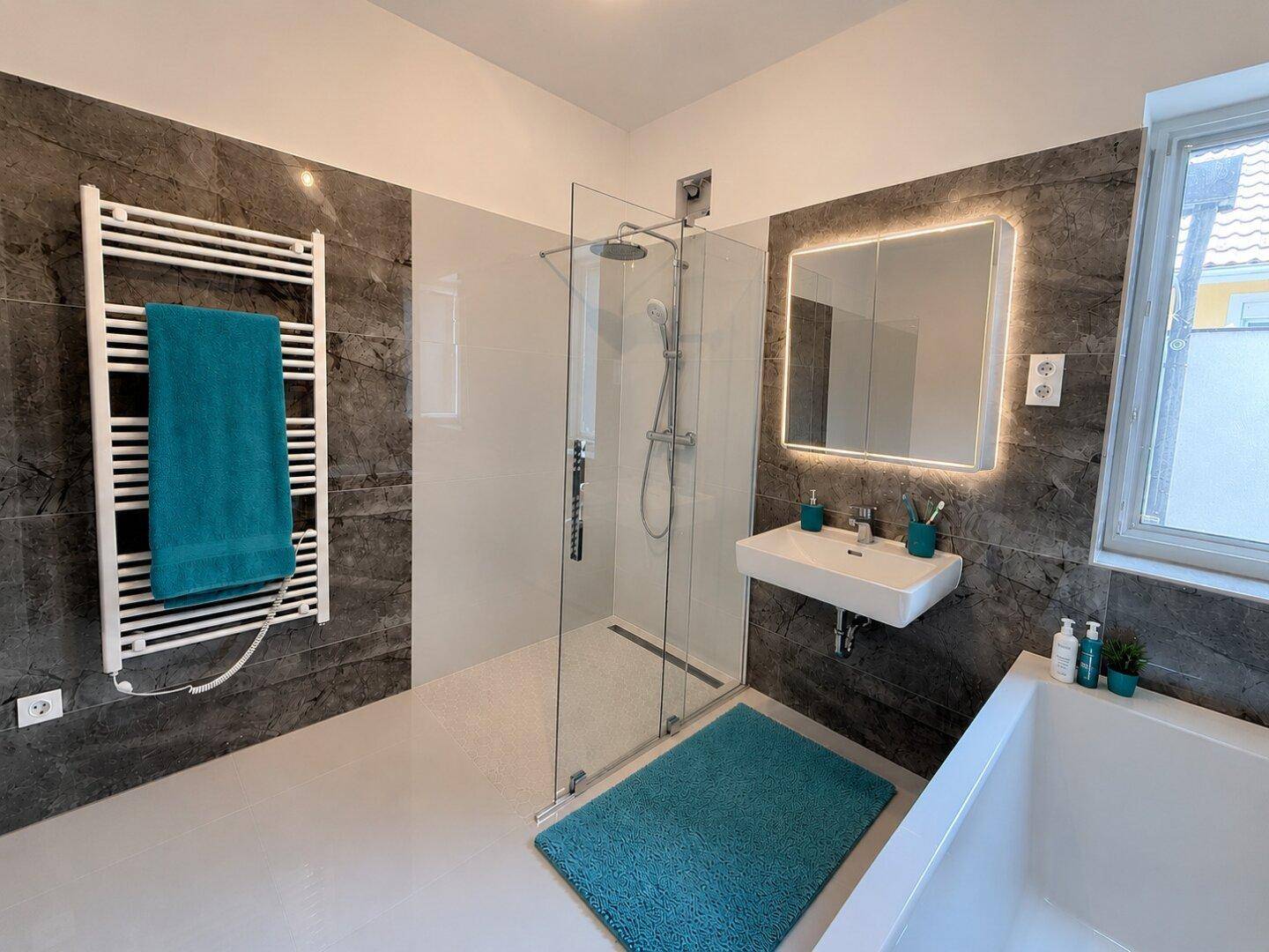 Modernes Badezimmer mit ebenerdiger Dusche, Badewanne, Waschbecken und beheiztem Handtuchhalter.