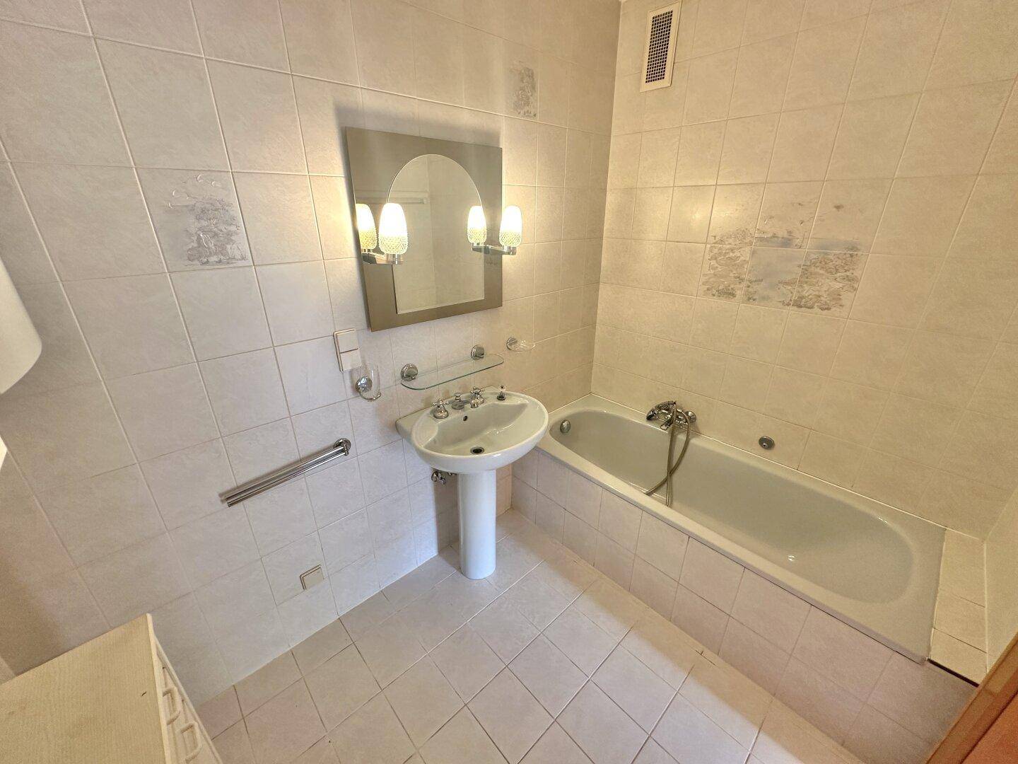 Badezimmer mit Badewanne, Waschbecken und hellen Fliesen im 80er-Jahre-Stil.