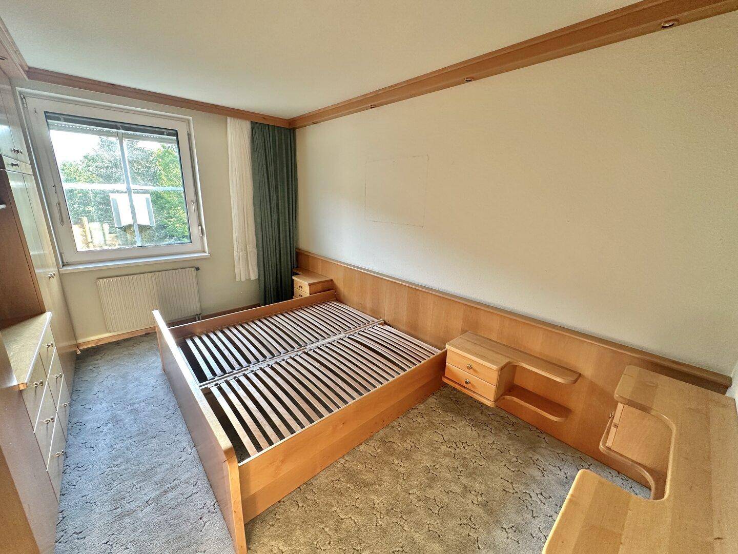 Schlafzimmer mit Holzvertäfelung, Teppichboden und Fensterblick ins Grüne.