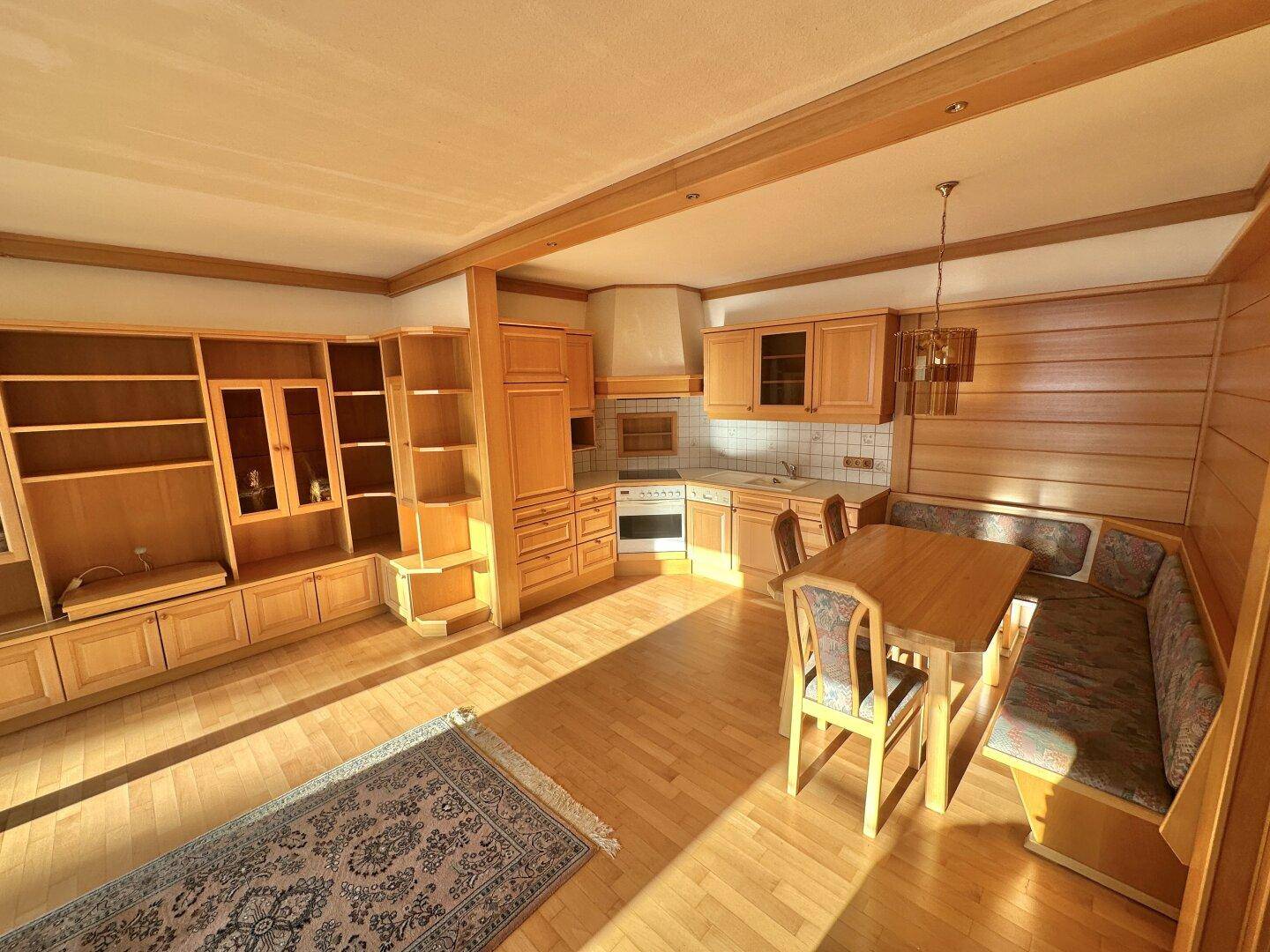 Geräumige Wohnküche mit Holzeinbauten, Essbereich und Parkettboden.