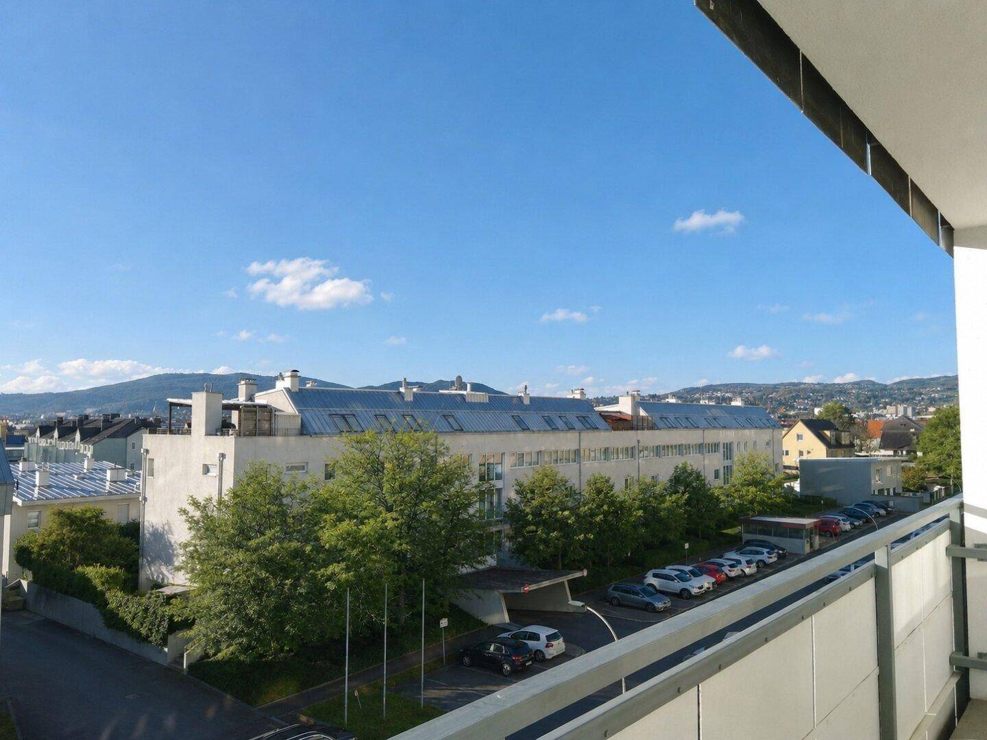Balkon mit weitem Blick über die Stadt, grüne Bäume und die umliegende Bebauung.