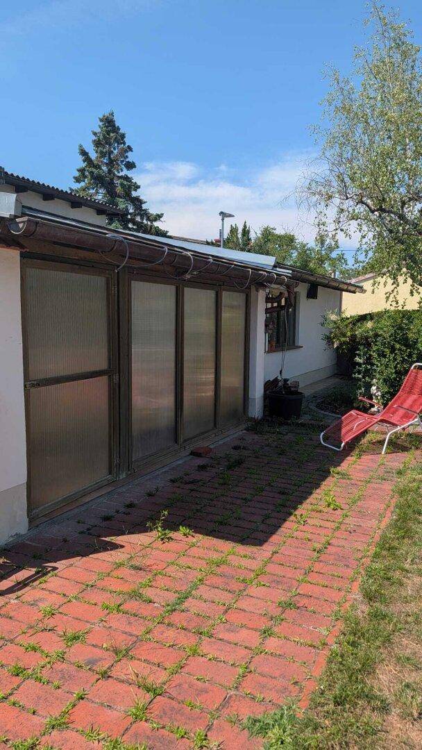 Ein Wintergarten mit Glasfront und rotem Ziegelpflaster bietet einen geschützten Außenbereich.