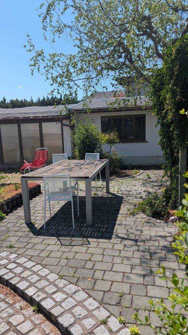 Eine gepflasterte Terrasse mit Esstisch und Stühlen bietet einen gemütlichen Bereich im Freien.