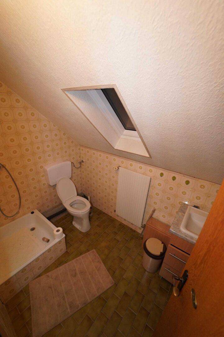 Badezimmer im Dachgeschoss mit schrägen Wänden, Badewanne, WC und einem Dachfenster.