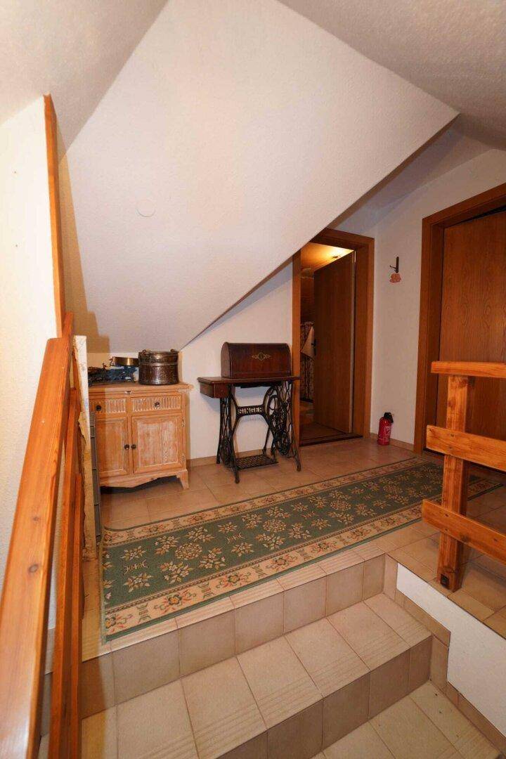 Ein Flur im Dachgeschoss mit Fliesenboden, Holztreppe und einer antiken Nähmaschine als Dekoration.