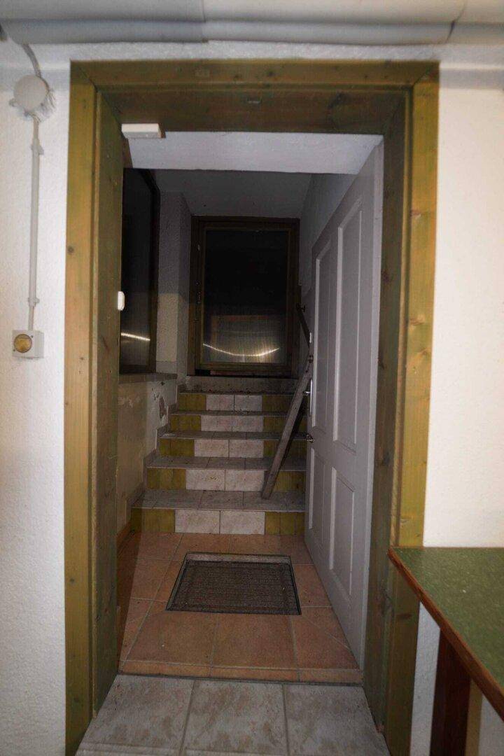 Eingang zum Keller mit gefliesten Stufen und einer Holztür, die in den unteren Bereich führt.