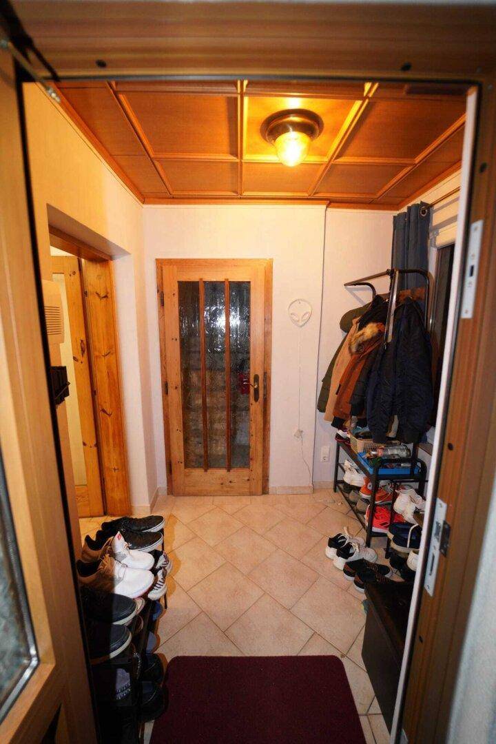 Eingangsbereich mit Fliesenboden, Holzdecke und praktischen Schuhregalen und Garderobe.