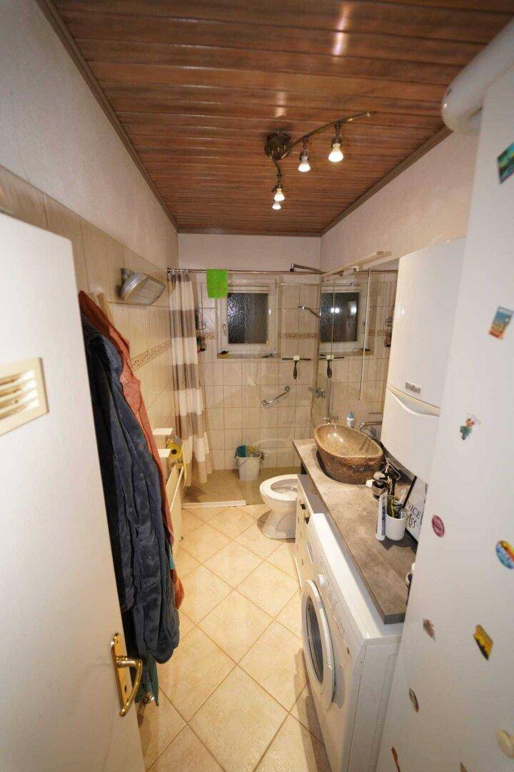 Badezimmer mit Dusche, WC, Waschbecken und integrierter Waschmaschine, funktional eingerichtet.