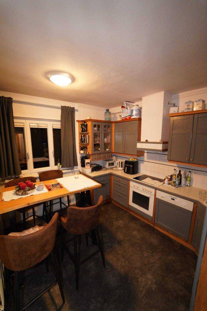 Gemütliche Küche mit Essbereich, grauen Schränken, Holzelementen und dunklem Boden.