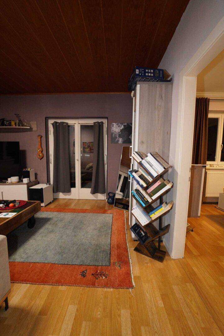 Wohnbereich mit Holzdecke, Parkettboden und Zugang zu einem weiteren Raum.