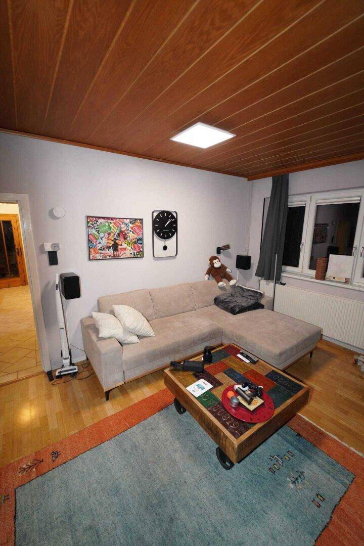 Gemütliches Wohnzimmer mit Holzboden, bequemer Eckcouch und dekorativer Holzdecke.