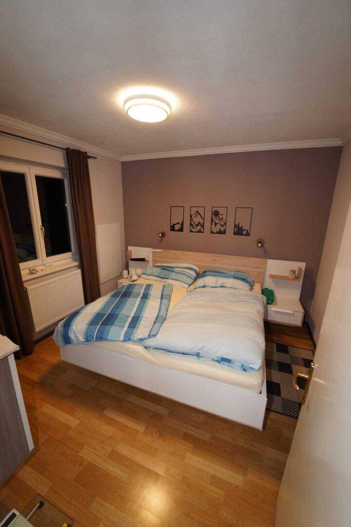 Schlafzimmer mit Holzboden, Doppelbett und einer Akzentwand in einem warmen Farbton.