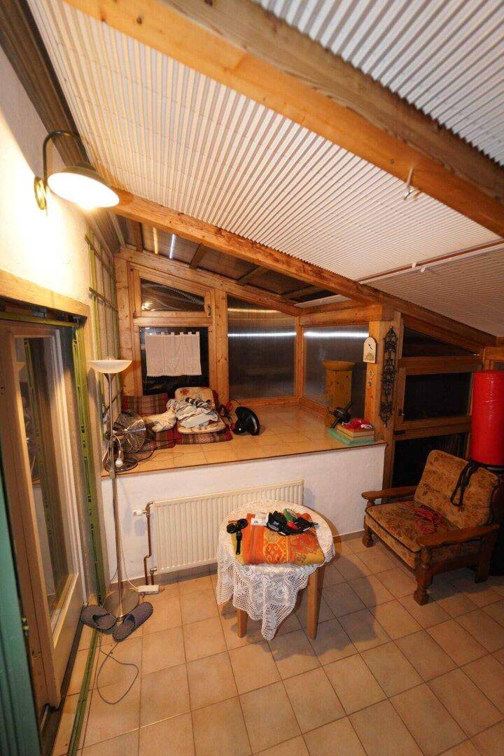 Wintergarten mit Sitzgelegenheit, Fliesenboden, Heizkörper und Holzkonstruktion.