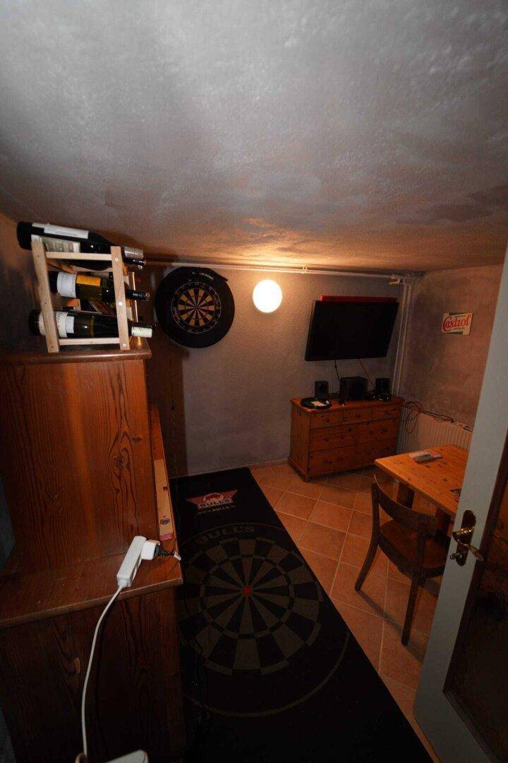 Kellerraum als Hobbyraum mit Dartscheibe, Fernseher und Holzmöbeln.