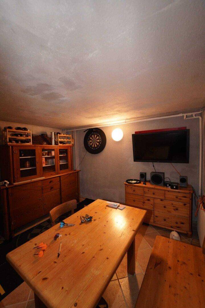 Kellerraum mit Holztisch, Schränken, Fernseher und Dartscheibe.