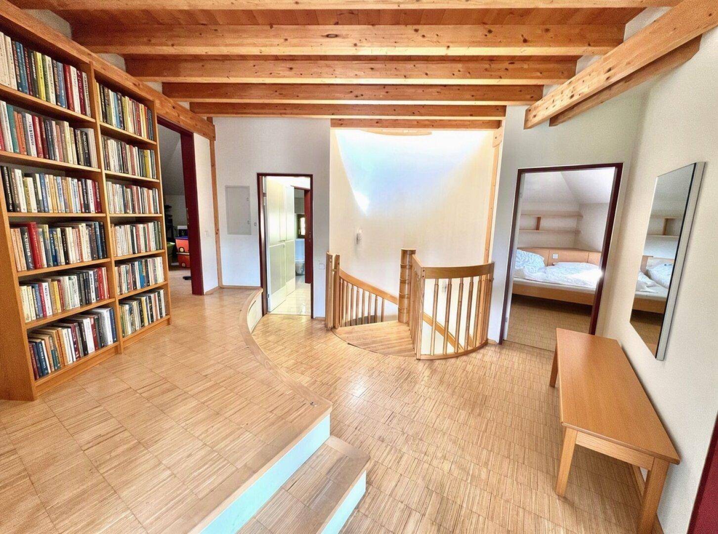 Heller Flur mit Holzbalkendecke, Parkettboden und einer großen Bücherwand.