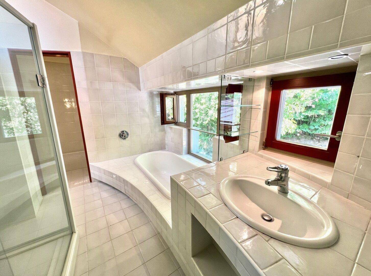 Helles Badezimmer mit weiß gefliesten Oberflächen, integrierter Badewanne und Dusche.