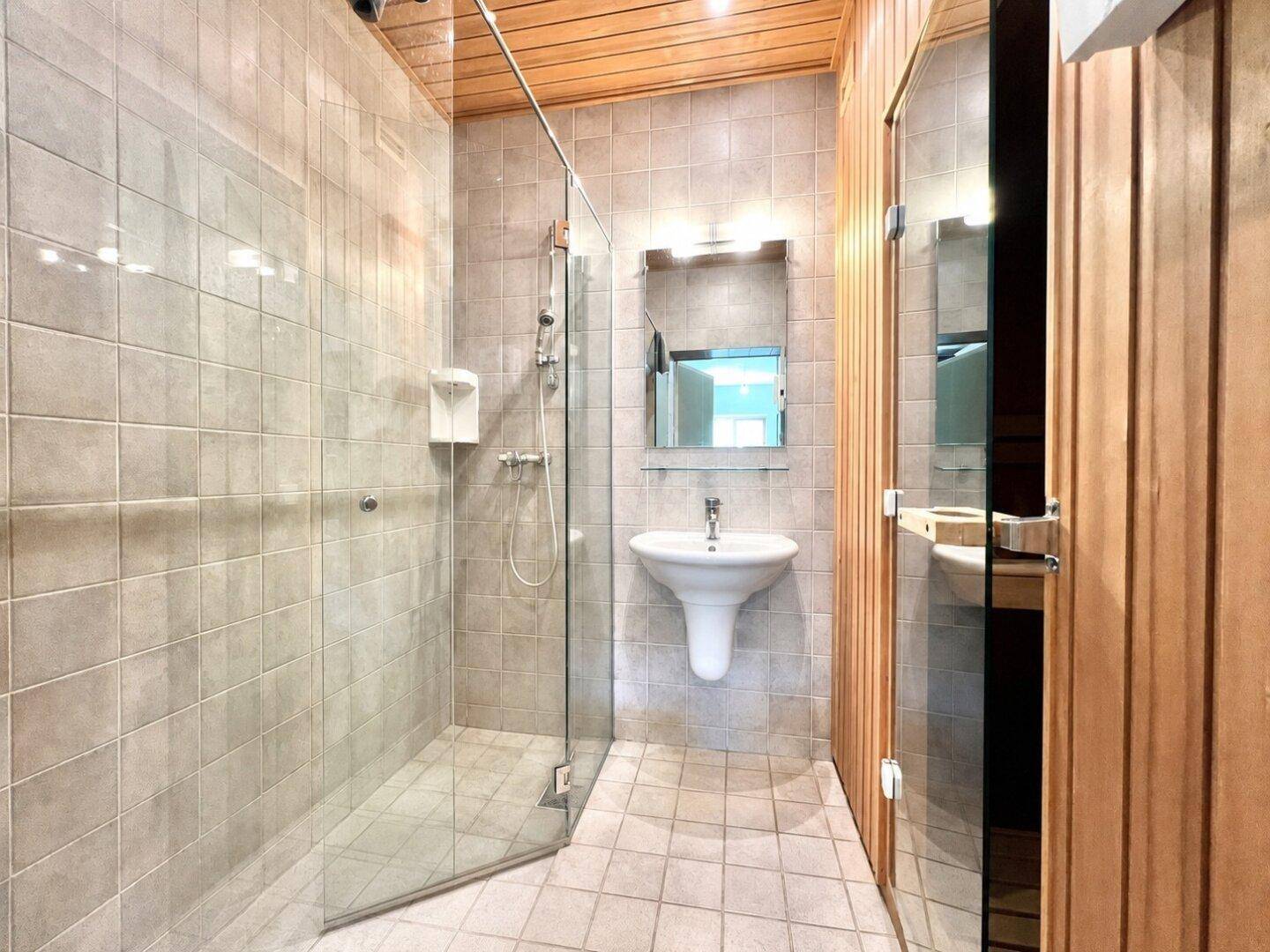 Modernes Badezimmer mit begehbarer Dusche, Waschbecken und Zugang zur Sauna.