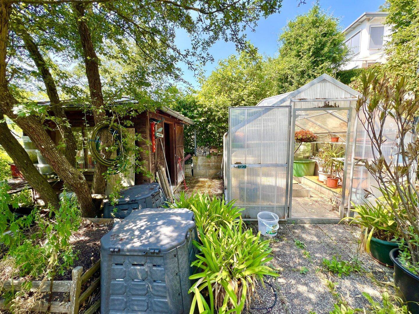 Funktionaler Gartenbereich mit Gewächshaus, Kompostbehältern und Obstbäumen.