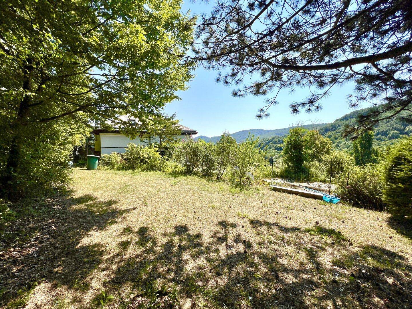 Weitläufige Rasenfläche im Garten mit Blick auf das Haus und die umliegende Natur.