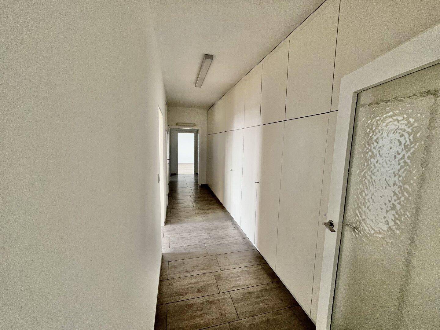 Heller Flur mit praktischen Einbauschränken entlang der Wand und Fliesenboden.