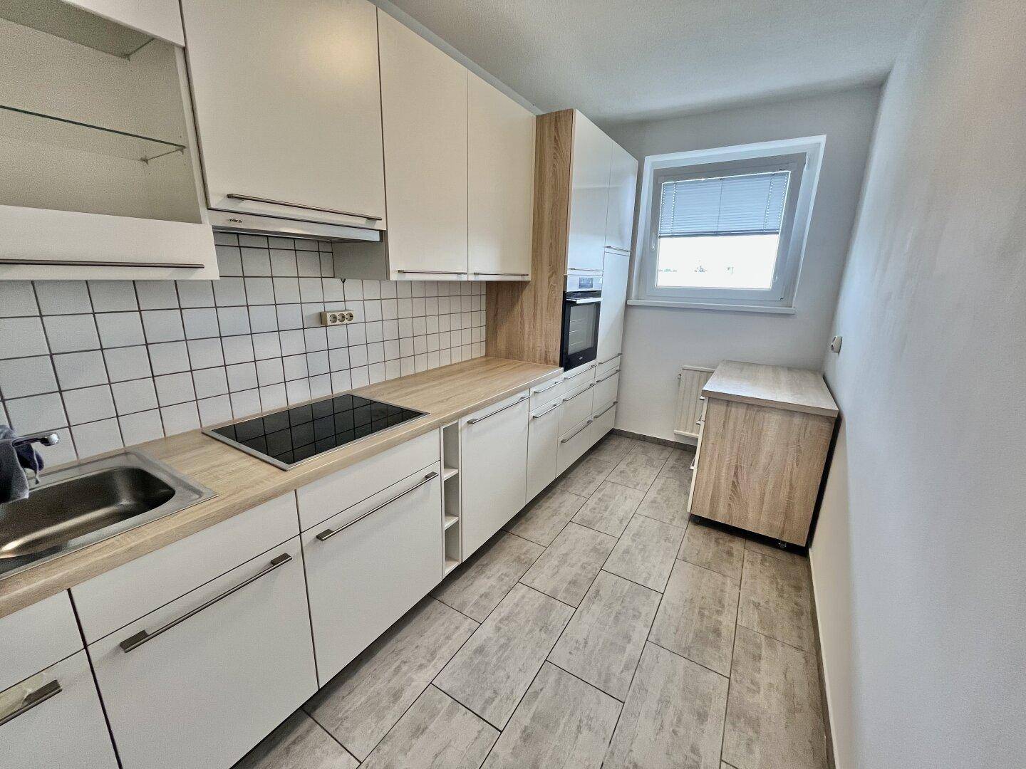 Funktionale Küche mit weißen Schränken, Holz-Arbeitsplatten, Induktionskochfeld und Fliesenboden.