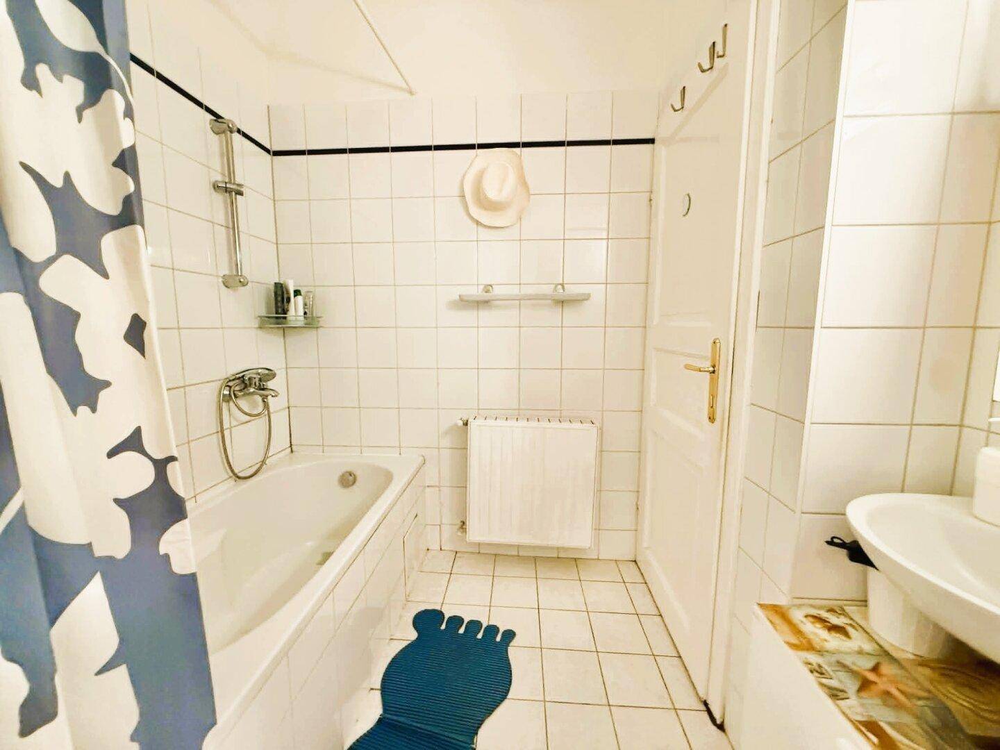 Badezimmer mit Badewanne, Duschvorhang und weißen Fliesen an Wänden und Boden.