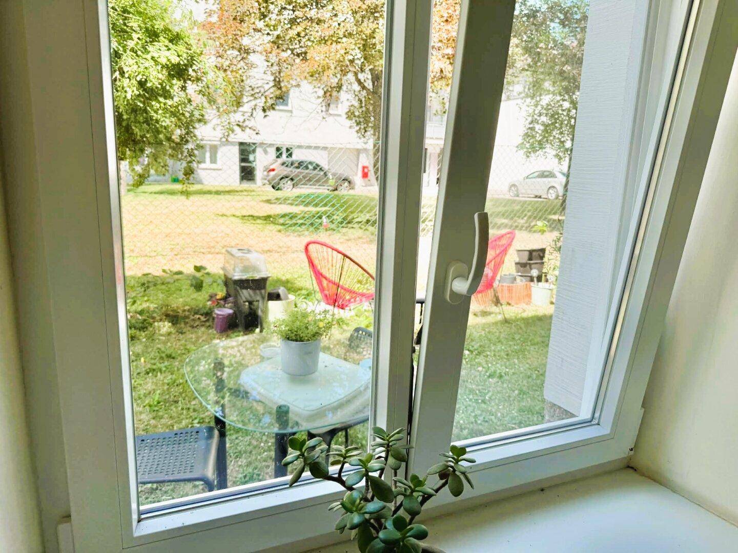 Blick aus dem Fenster auf einen grünen Garten mit Sitzgelegenheiten und Grill.