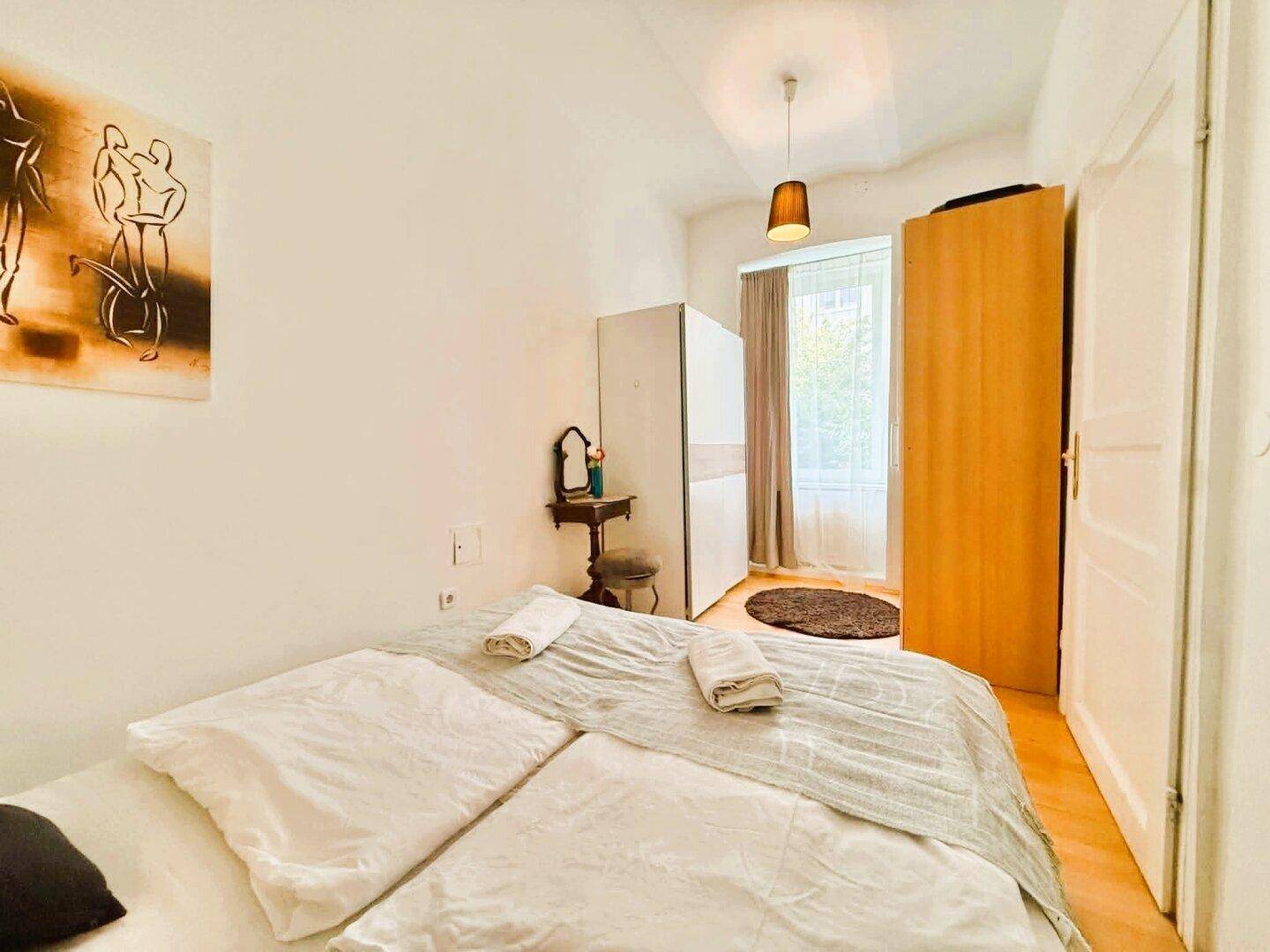 Helles Schlafzimmer mit Holzboden, Doppelbett und einem Fenster mit Blick ins Grüne.