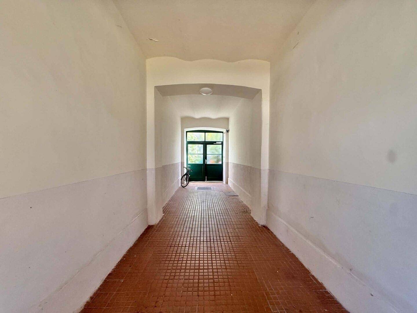 Langer Flur mit Fliesenboden und einem Blick zum Ausgang des Gebäudes.