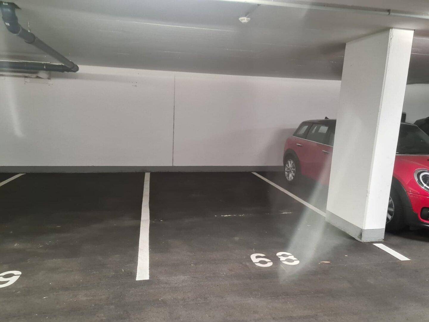 Nahaufnahme des Tiefgaragenstellplatzes 68 mit einem geparkten roten Fahrzeug und sauberer Umgebung.