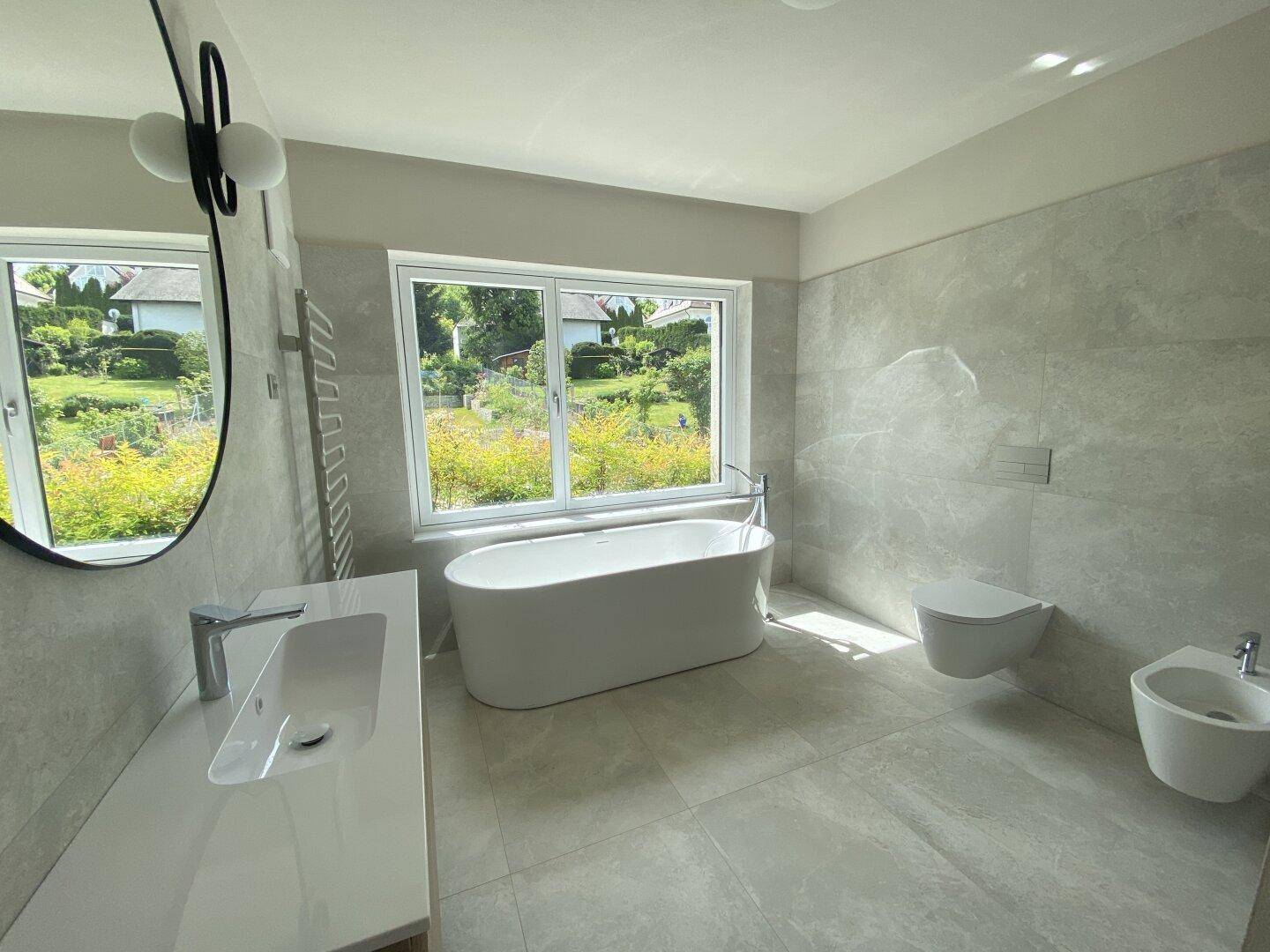 Modernes Badezimmer mit freistehender Badewanne, Waschtisch, Toilette und großem Fenster.