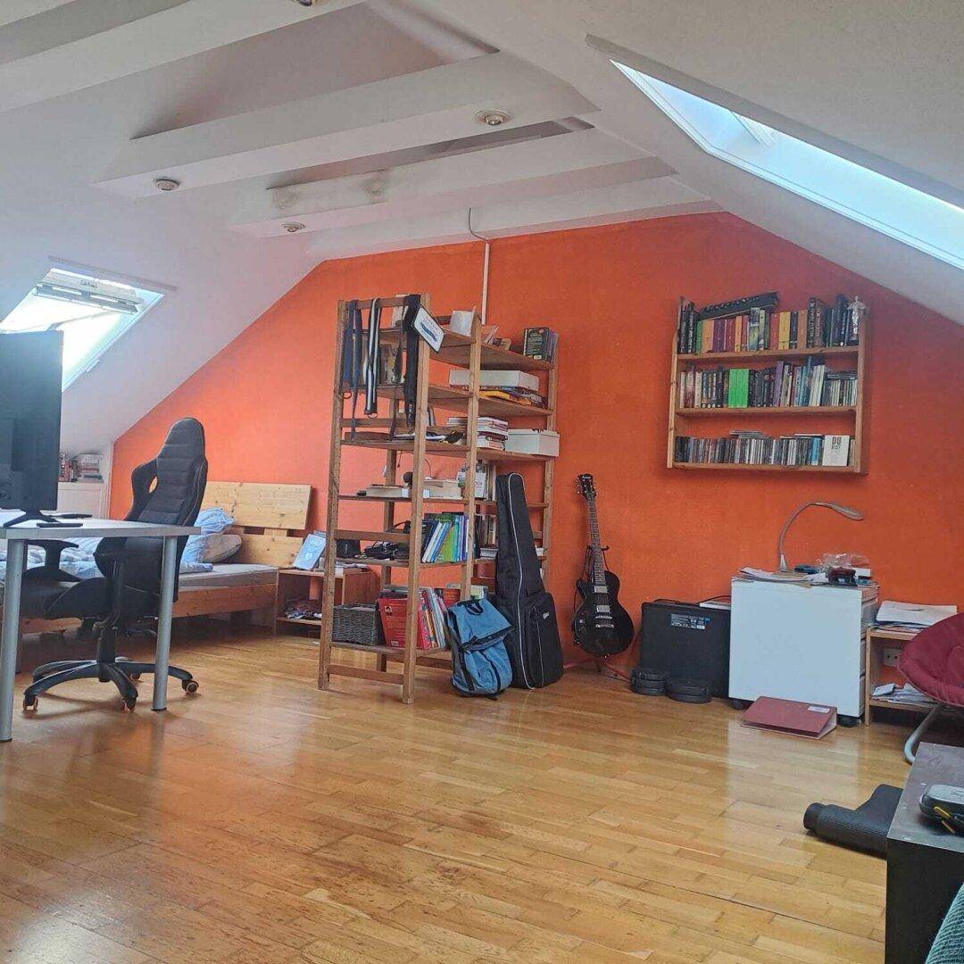 Geräumiger Dachbodenraum mit Schrägen, Dachfenstern, Holzboden und orangefarbener Wand.