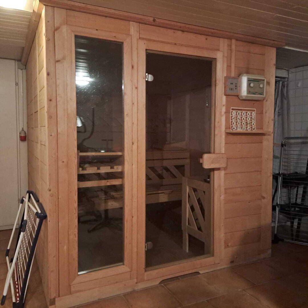 Private Sauna aus hellem Holz mit Glastür und Steuerungselementen im Kellerbereich.