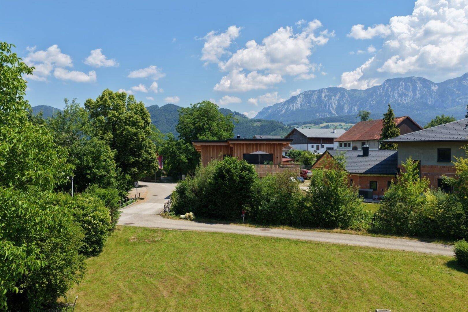 Weitläufiger Blick über grüne Wiesen und die Bergkette in ländlicher Umgebung.