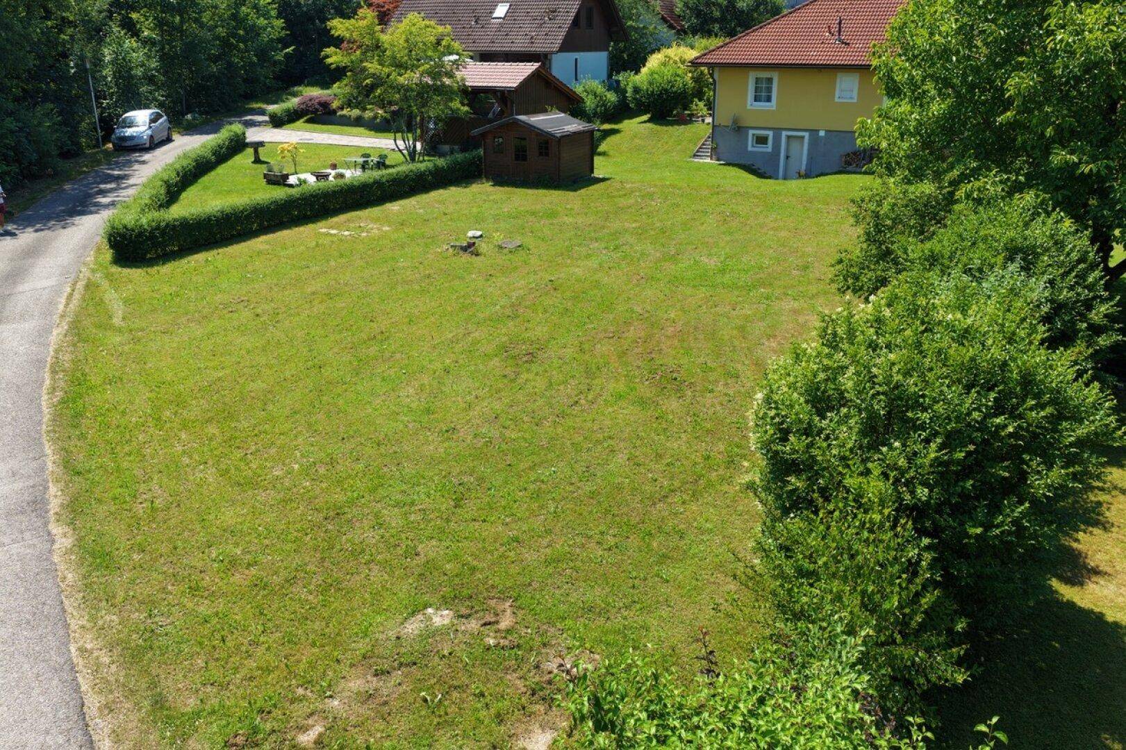Großes, gepflegtes Rasengrundstück mit Hecke und kleinem Gartenhaus.