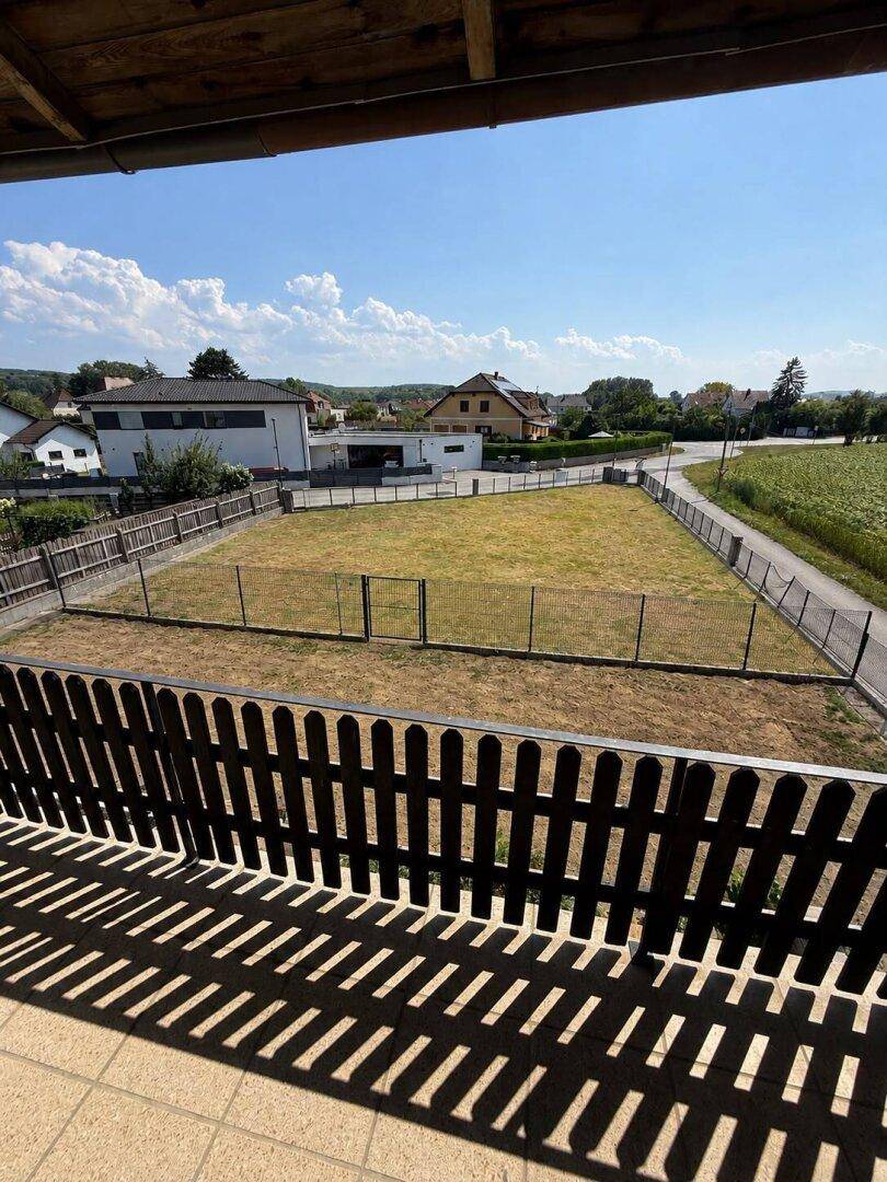 Blick vom Balkon auf ein großes, eingezäuntes Grundstück und die umliegende Landschaft.