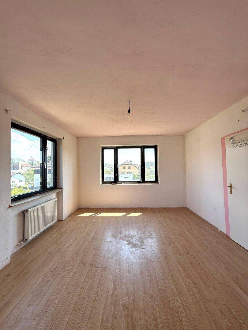 Helles, leeres Zimmer mit Holzboden und mehreren Fenstern, bereit zur Renovierung.