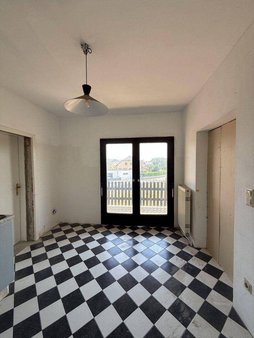 Helle Küche mit Schachbrettmuster-Fliesenboden und Zugang zum Balkon.