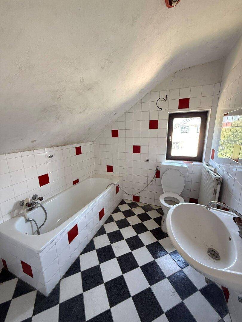 Badezimmer mit Badewanne, WC und Waschbecken unter einer Dachschräge.