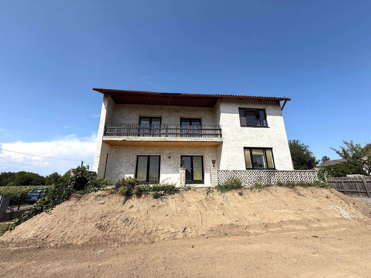 Vorderansicht des Hauses auf einem erhöhten Grundstück mit Balkon und Terrasse.