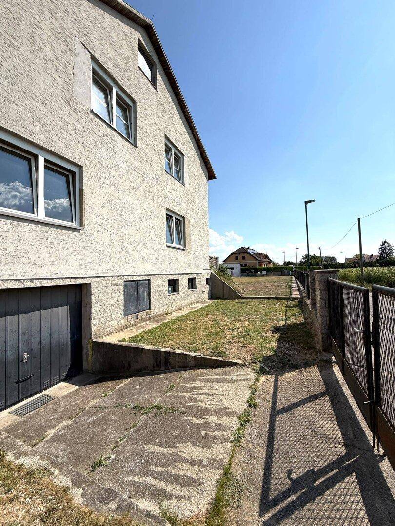Seitenansicht des Hauses mit Garagenzufahrt und angrenzendem Grundstück.